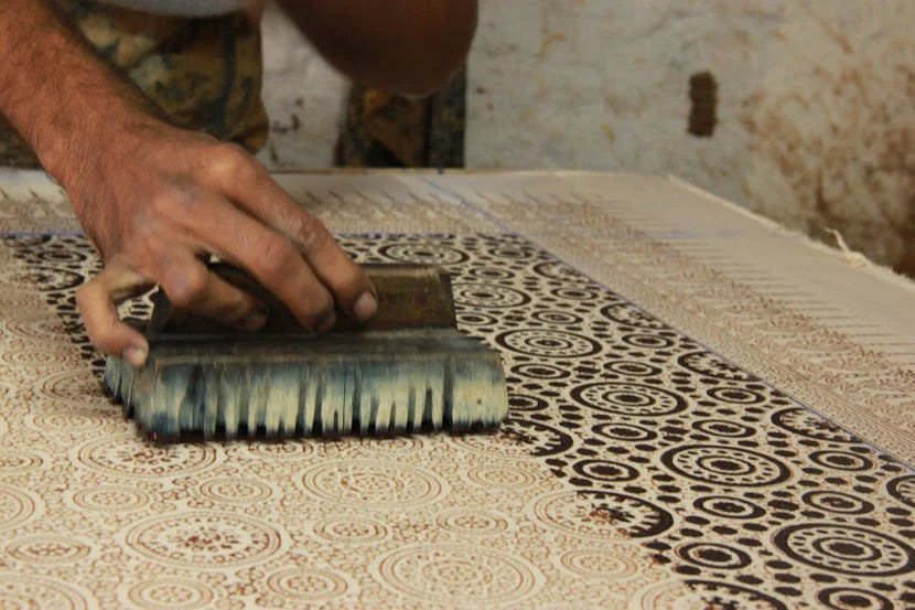 Artisan demonstrating hand block printing techniques on fabric in a traditional workshop setting